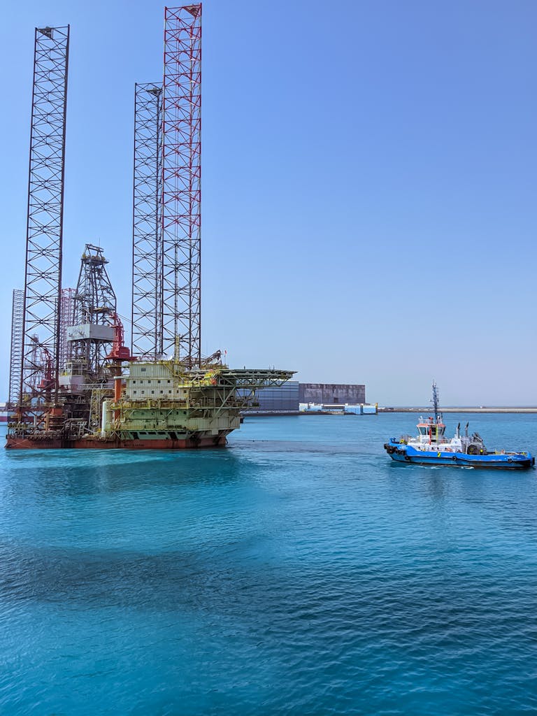 An offshore oil rig and a tugboat in Ras Laffan Harbor, Qatar, with clear blue sea and sky.